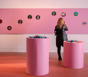 Woman looking at art in gallery with pink wall and pedestals.