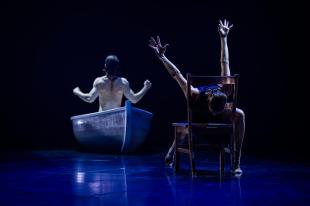 A man is sitting in a boat with his back to us. A woman is sitting on a chair with her face down.
